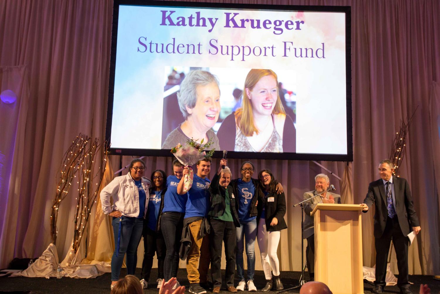 Mrs. Krueger celebrates the new Student Support Fund with students on stage at the auction. The fund is now named in Krueger's honor.